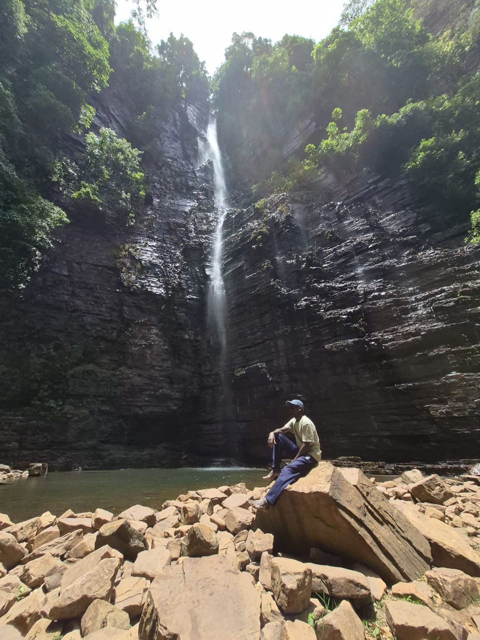 Un homme assis sur les rochers au pied de la cascade de Dindéfélo