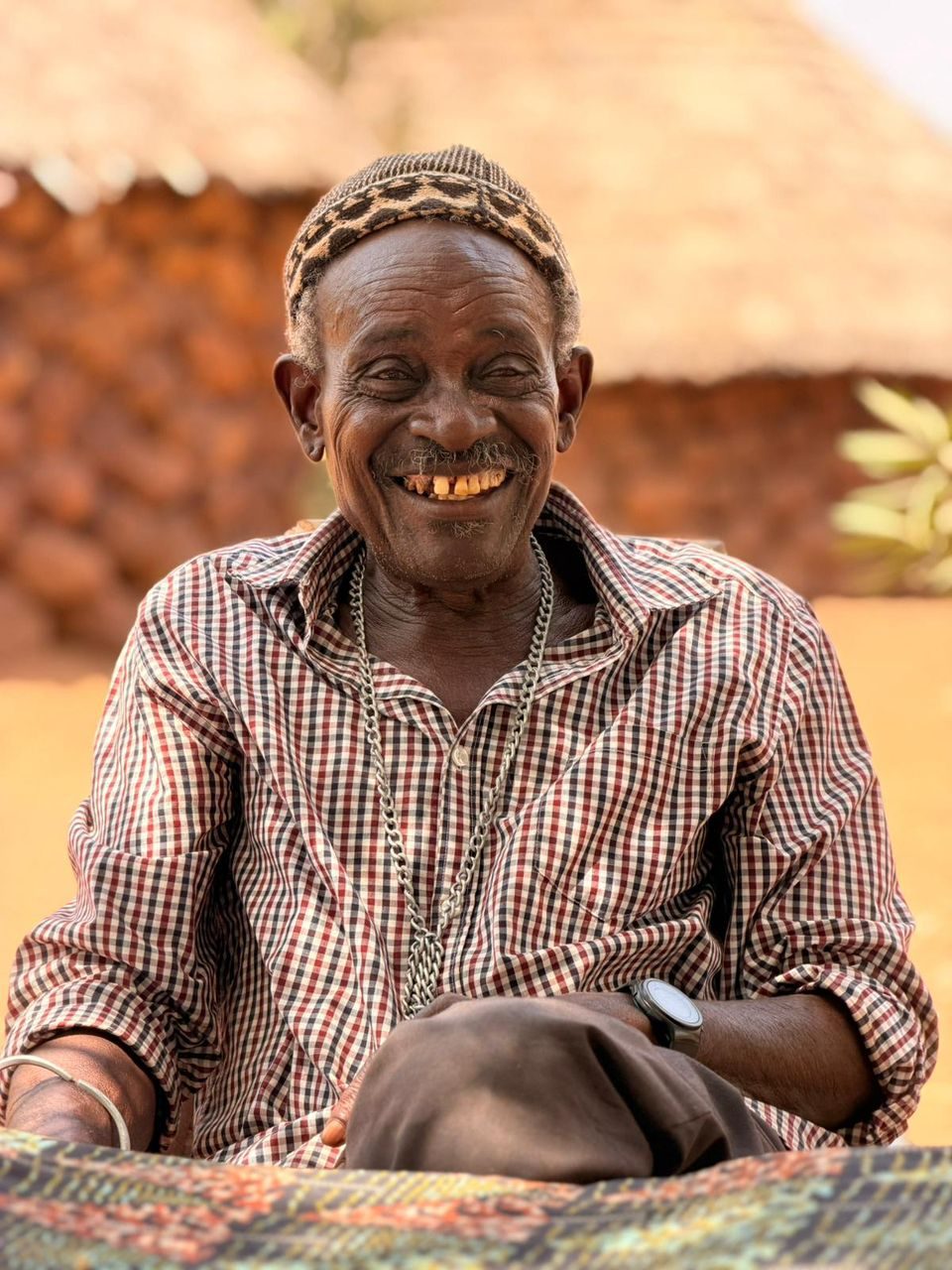 Portrait souriant du chef de village, devant une case