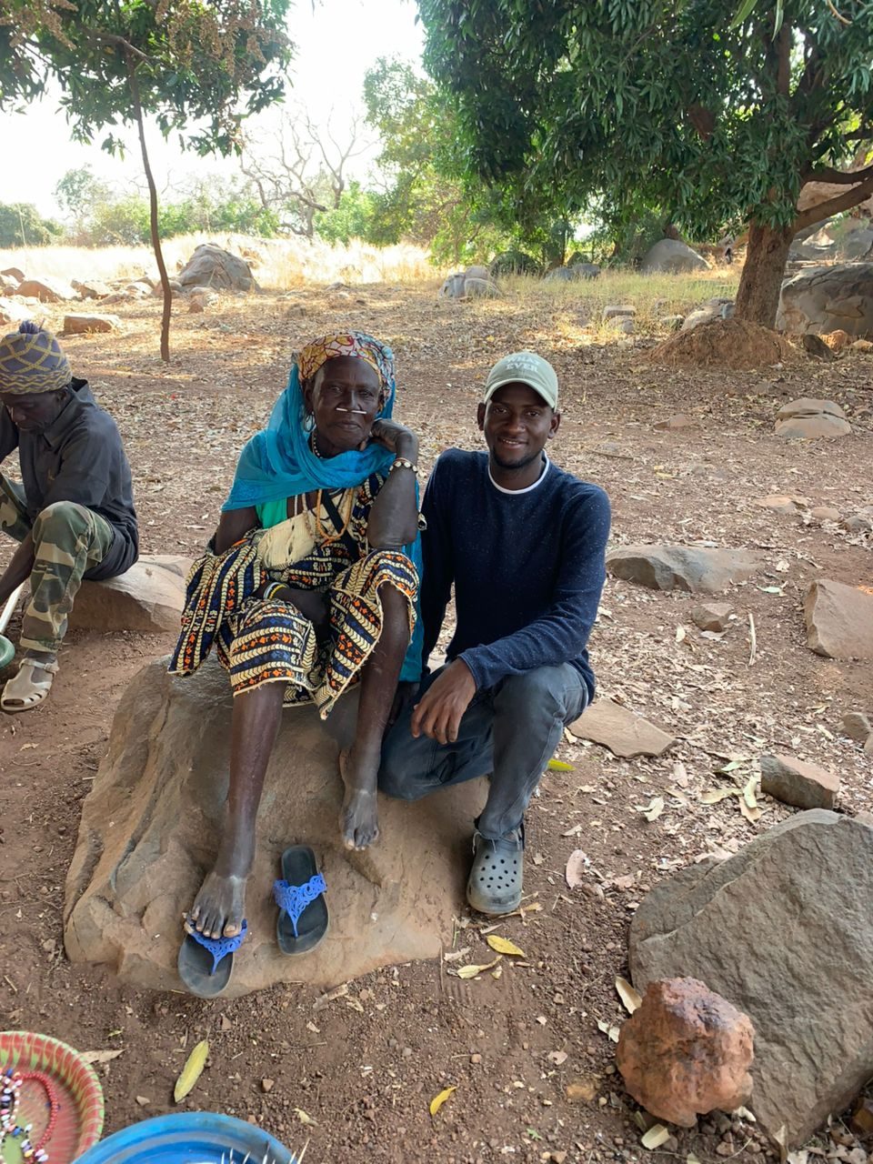 Abdourahmane assis auprès d'une femme âgée, devant sa concession